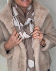 Woman wearing a beige faux fur coat and an animal print scarf