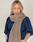 Woman wearing a taupe knitted scarf and blue top