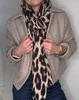 Woman wearing a beige coat, blue jeans, and a taupe leopard print scarf
