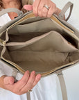 woman holding a beige leather tote handbag demonstrating the interior