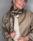 Woman wearing a beige trench coat with a taupe leopard print scarf