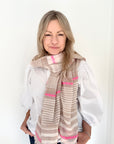 Woman wearing a white shirt and taupe and pink stripped scarf.