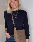 Woman wearing a black top and blue jeans with a taupe suede crossbody/ shoulder bag