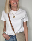 Woman wearing a white t-shirt, blue jeans, and carrying a taupe raffia clutch/ crossbody handbag.