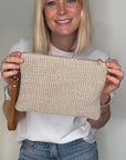 Woman wearing a white t-shirt, blue jeans, and carrying a taupe raffia clutch/ crossbody handbag.