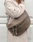 A woman wearing an XL taupe crossbody bag with silver hardware and an adjustable strap.