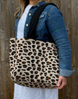 Person holding a leopard print tote bag against a wooden fence.