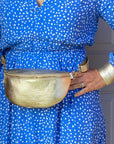 A person wearing a blue dotted dress with a gold leather crossbody bag with a detachable strap.