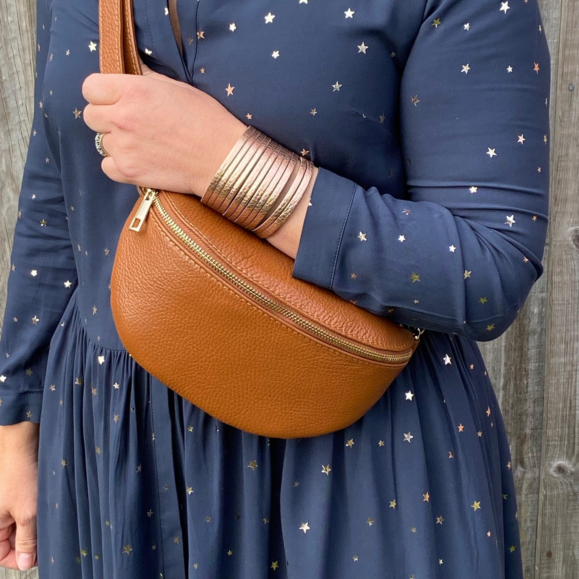 A person wearing a navy dress with gold stars is carrying a dark tan leather crossbody bag with a gold-colored zipper.