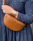 A person wearing a navy dress with gold stars is carrying a dark tan leather crossbody bag with a gold-colored zipper.