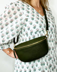 a woman wearing a large khaki crossbody/ waist bag, with gold accented hardware.