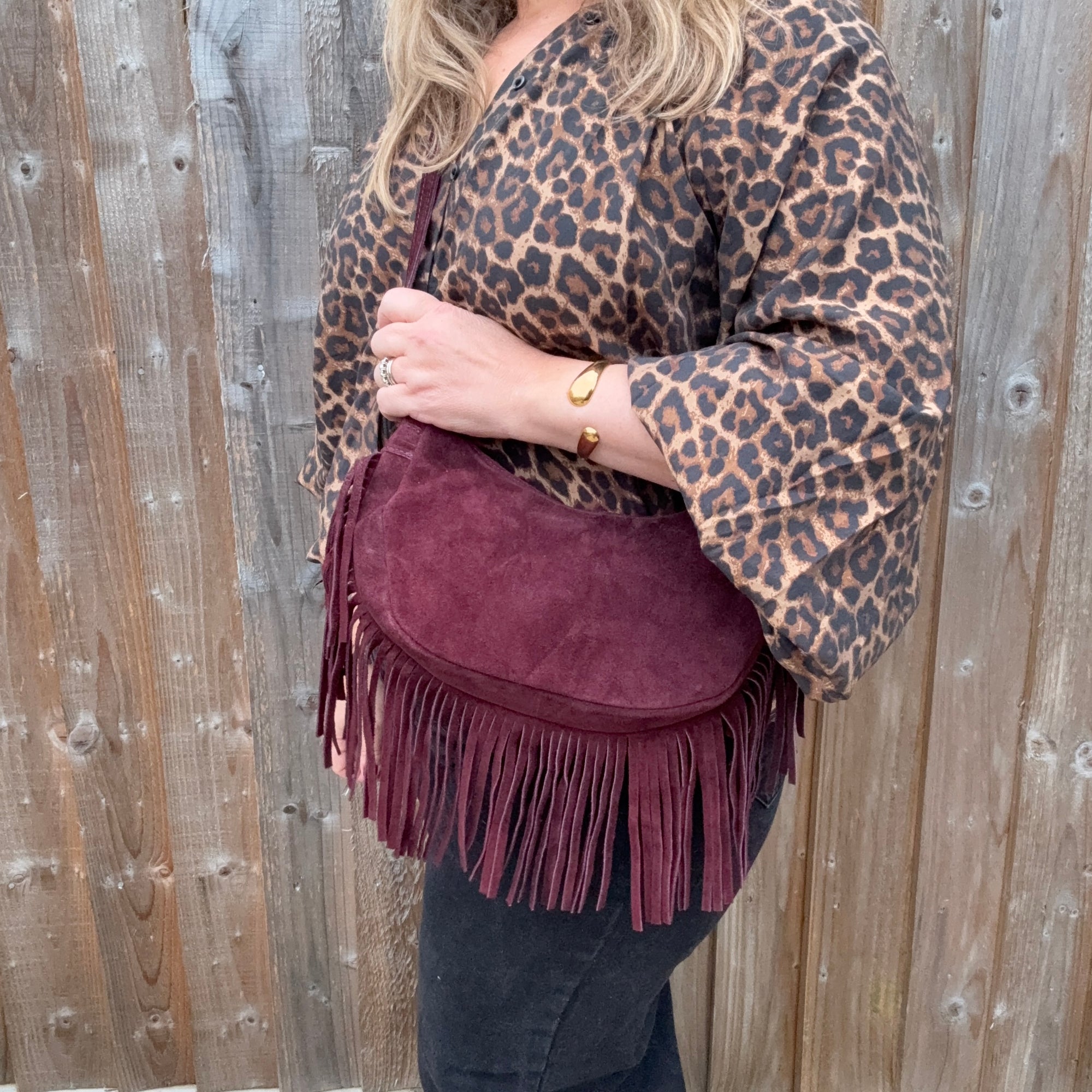 Person wearing a leopard print top and holding a burgundy suede crossbody bag with fringe detail
