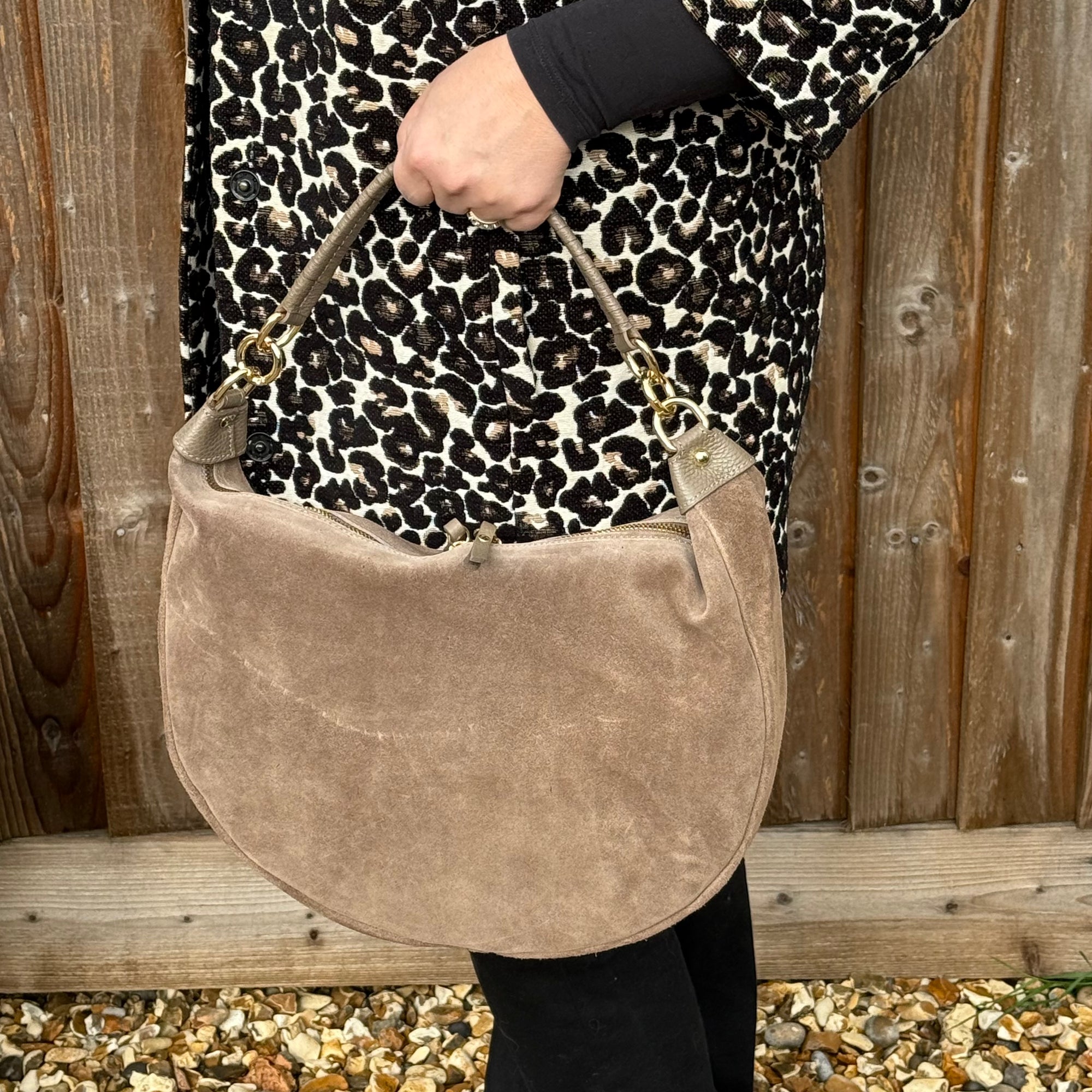 Person holding a taupe suede handbag with a leopard print coat s