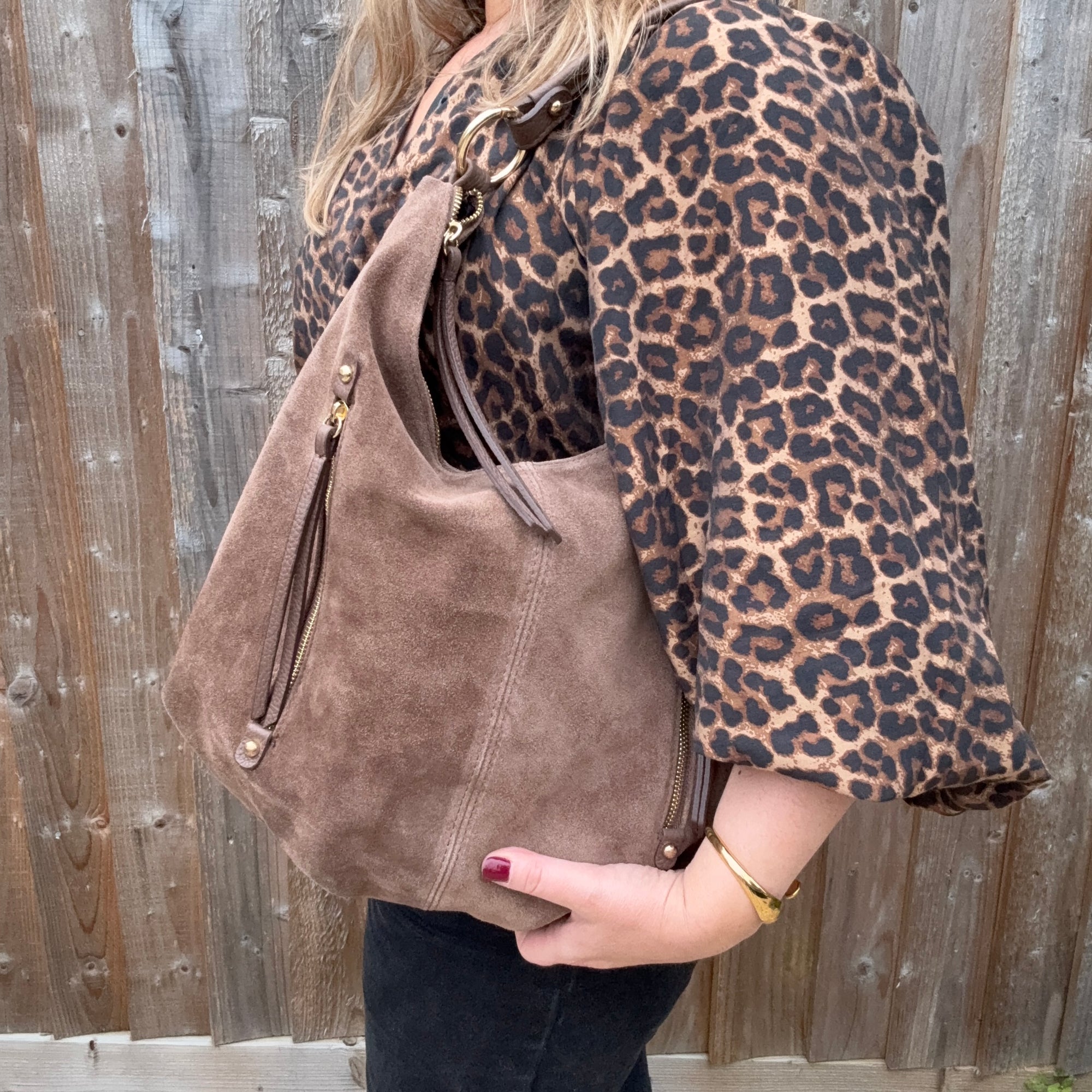 Person wearing a leopard print coat holding a taupe suede handbag 