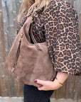 Person wearing a leopard print coat holding a taupe suede handbag 