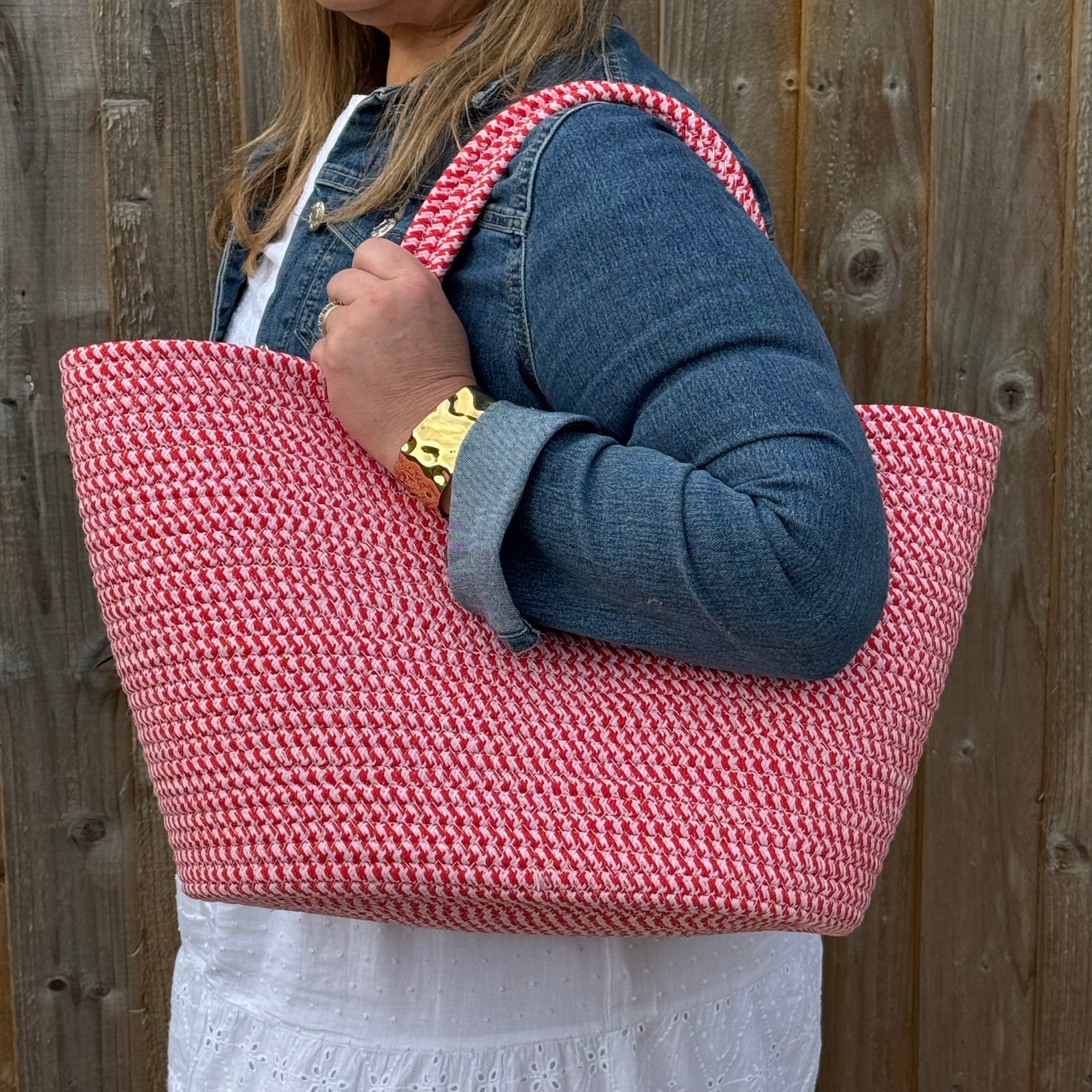 Person holding a red woven bag with a wooden fence background