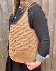 Woman wearing a denim jacket and black skirt, holding a beige and black woven raffia shoulder handbag.