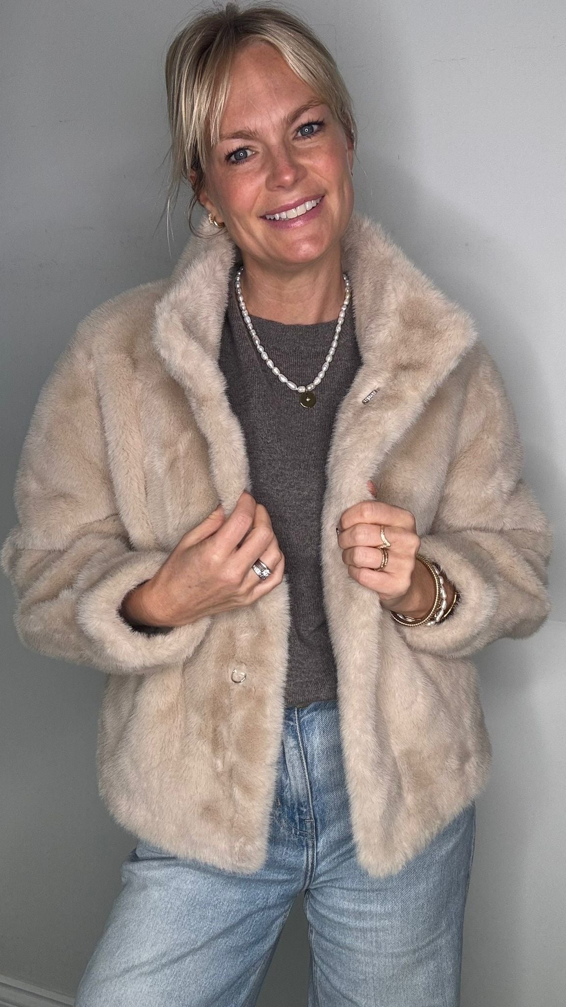 Woman wearing a beige faux  fur coat over a grey jumper 