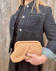 Woman wearing a denim jacket and black dress, holding a beige knitted cloud bag. 