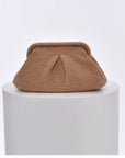 Beige knitted cloud clutch bag on a white pedestal with a light gray background