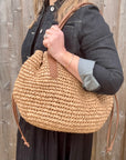 Woman wearing a black dress and denim jacket, holding a beige raffia shoulder handbag. 