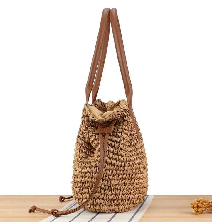 Woven straw bag with brown leather straps on a white background