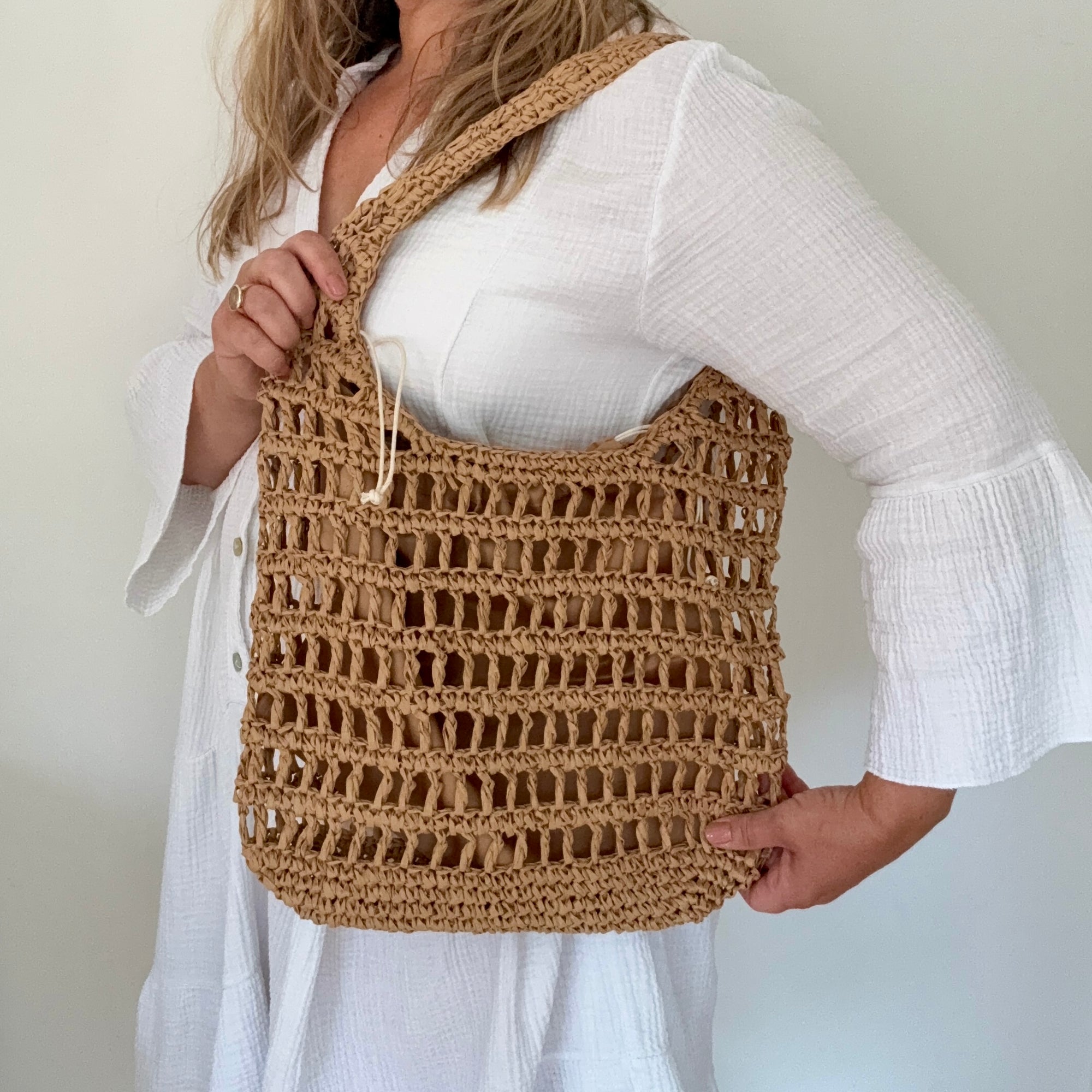 woman holding a brown woven bag against a plain background