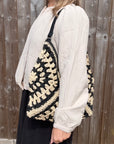 Woman wearing a white shirt holding a black and cream raffia tote bag.