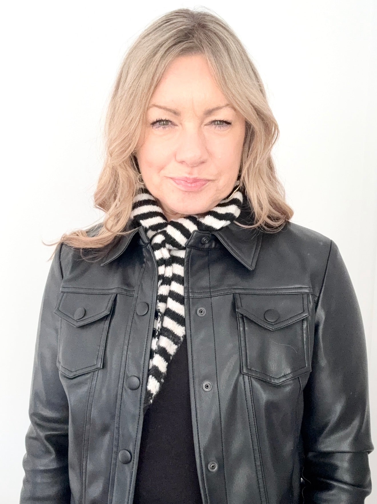 Woman wearing a black leather jacket and a black and white striped scarf on a white background