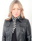Woman wearing a black leather jacket and a black and white striped scarf on a white background