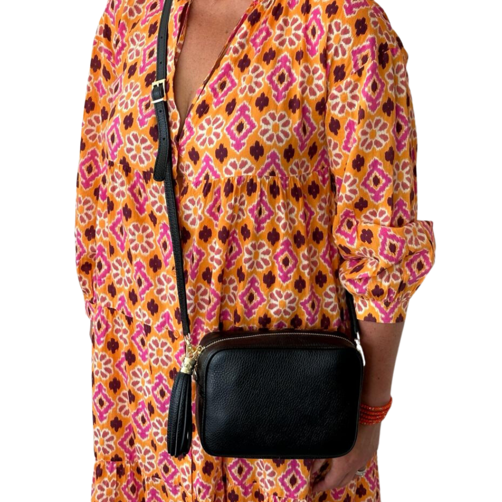 a woman holding a black leather crossbody bag with a tassel.
