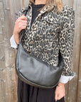 Woman wearing a leopard print jacket holding a black crossbody handbag.