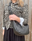 Woman wearing a leopard print jacket holding a black crossbody handbag.