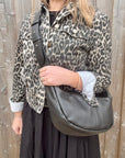 Woman wearing a leopard print jacket holding a black crossbody handbag.