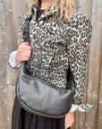 Woman wearing a leopard print jacket holding a black crossbody handbag.