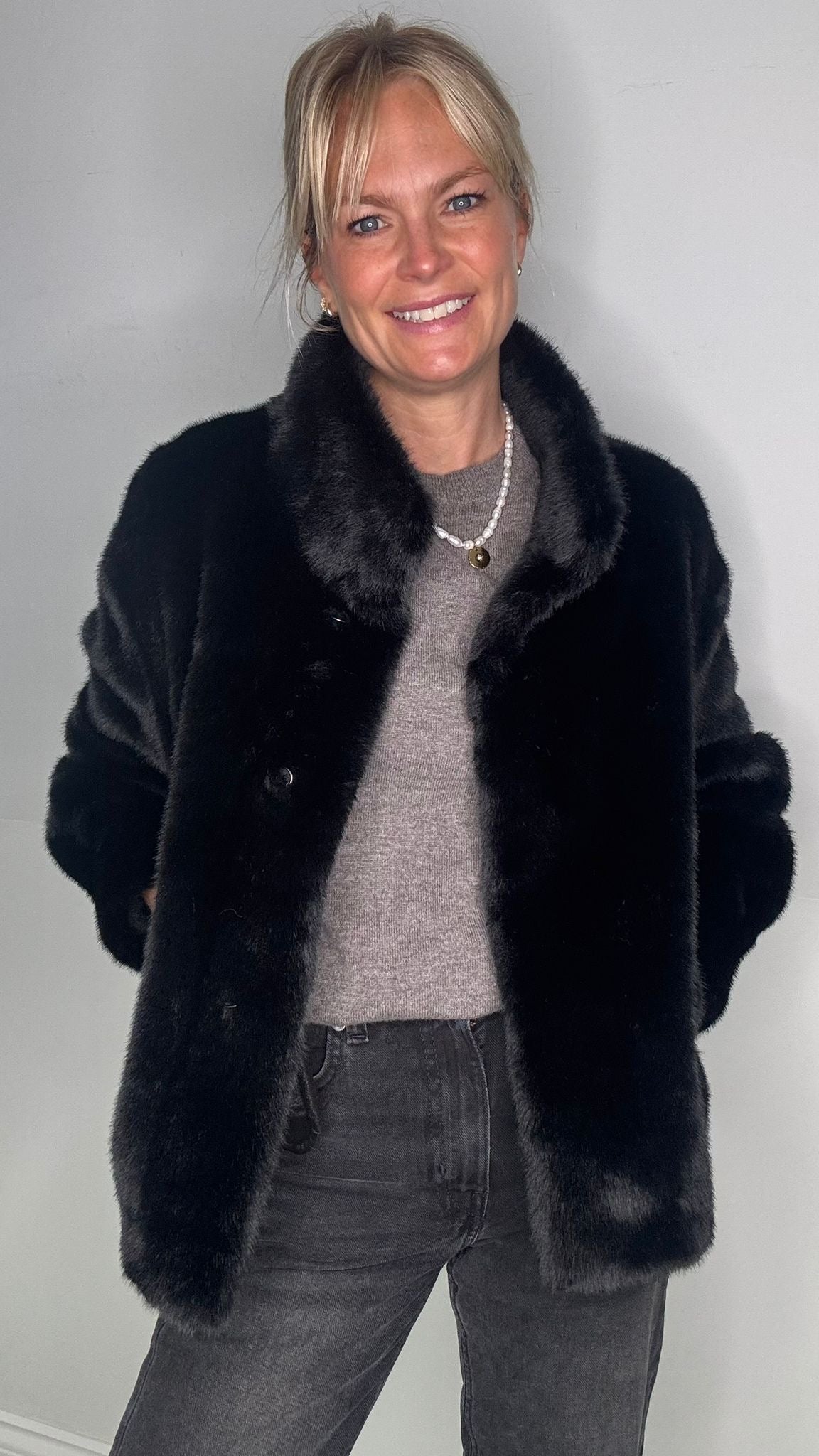woman with blonde hair  wearing a black faux fur coat and grey jeans 
