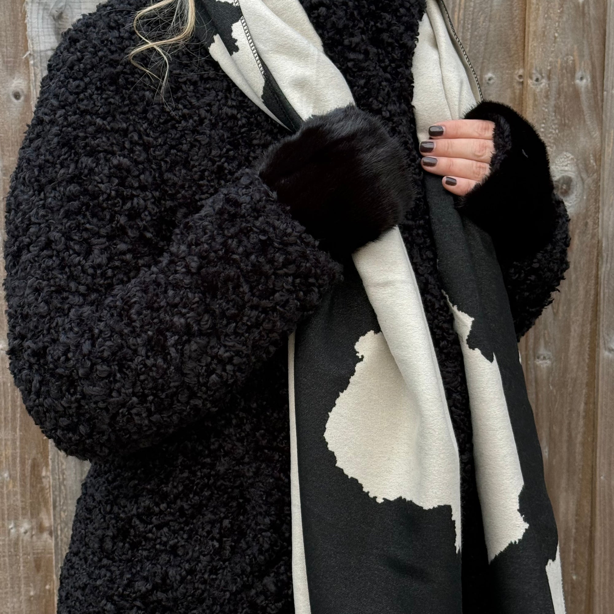 woman wearing a black coat with a patterned scarf and faux fur wrist warmers. 