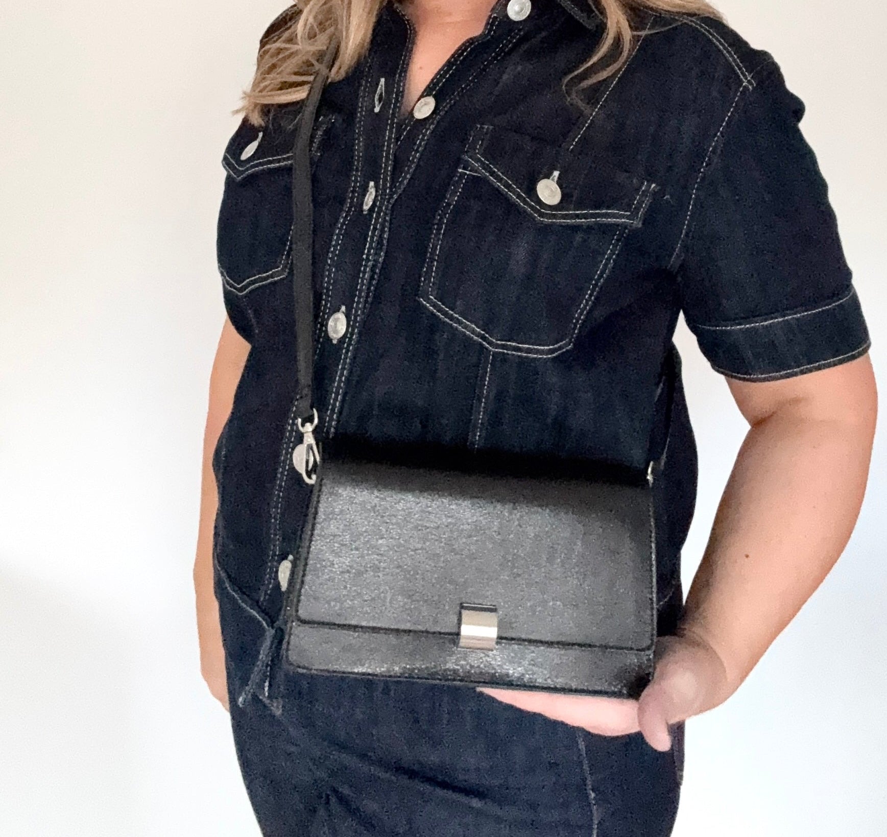 woman wearing a dark denim jacket with a black faux leather clutch/ crossbody handbag.