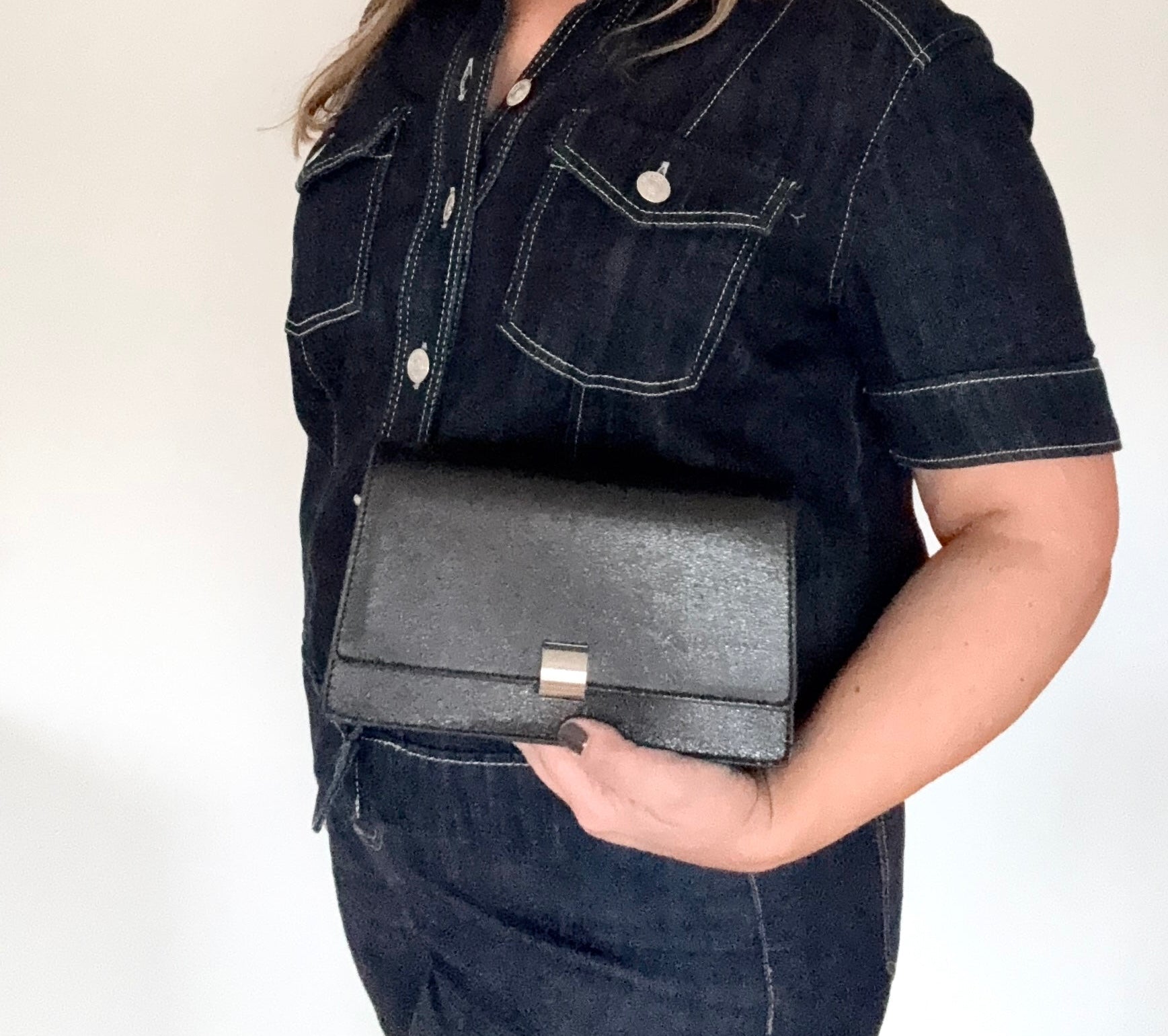 woman wearing a dark denim jacket holding a black faux leather clutch/ crossbody bag 