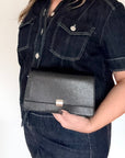woman wearing a dark denim jacket holding a black faux leather clutch/ crossbody bag 