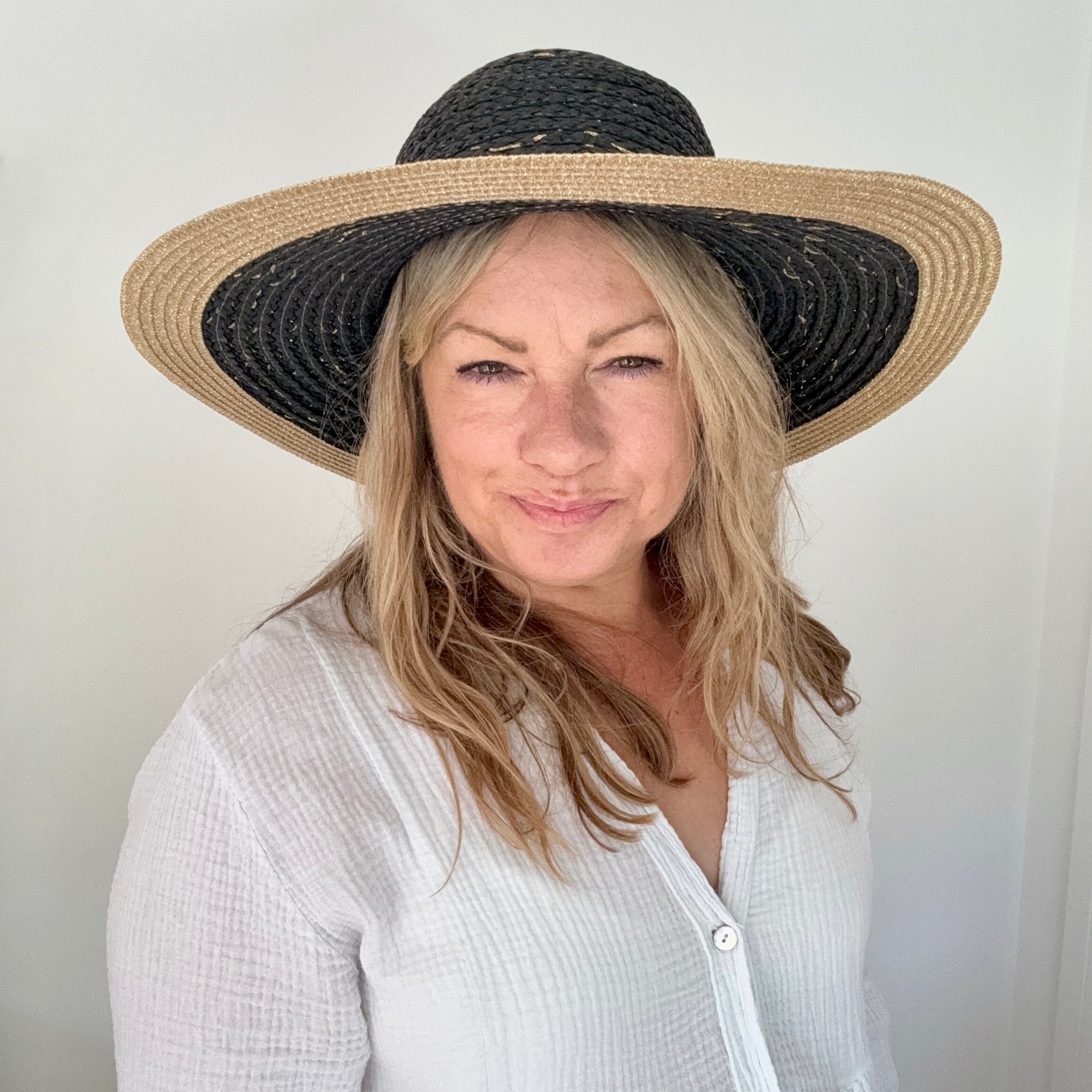 Woman wearing a black and beige straw hat against a plain background