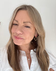 Woman  wearing a white shirt and black and grey beaded gold hoop earrings. 