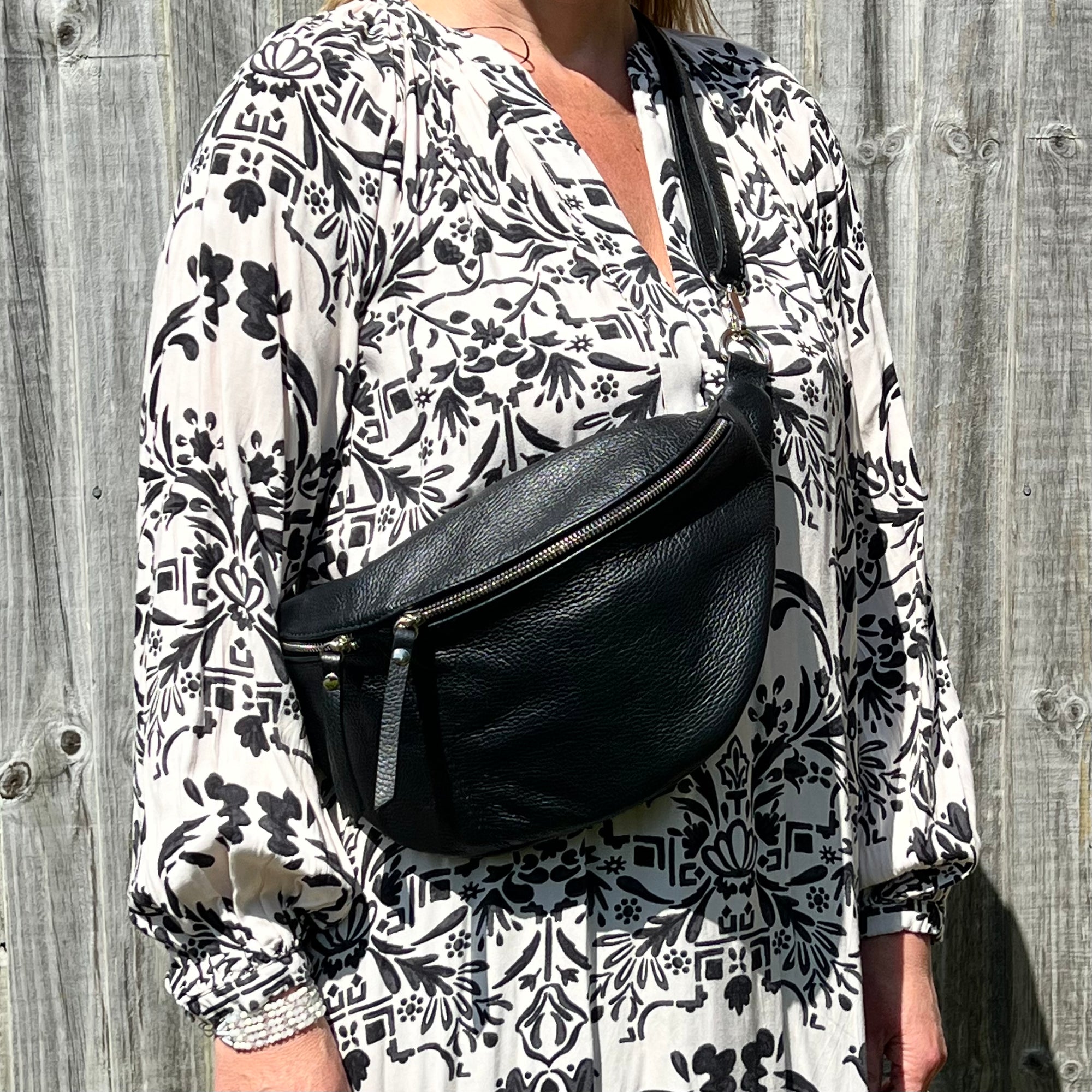 A person wearing a black large crossbody bum bag with an adjustable, detachable leather strap and multiple zip pockets.