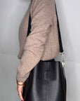 lady wearing a beige cardigan and holding a black leather bucket bag 