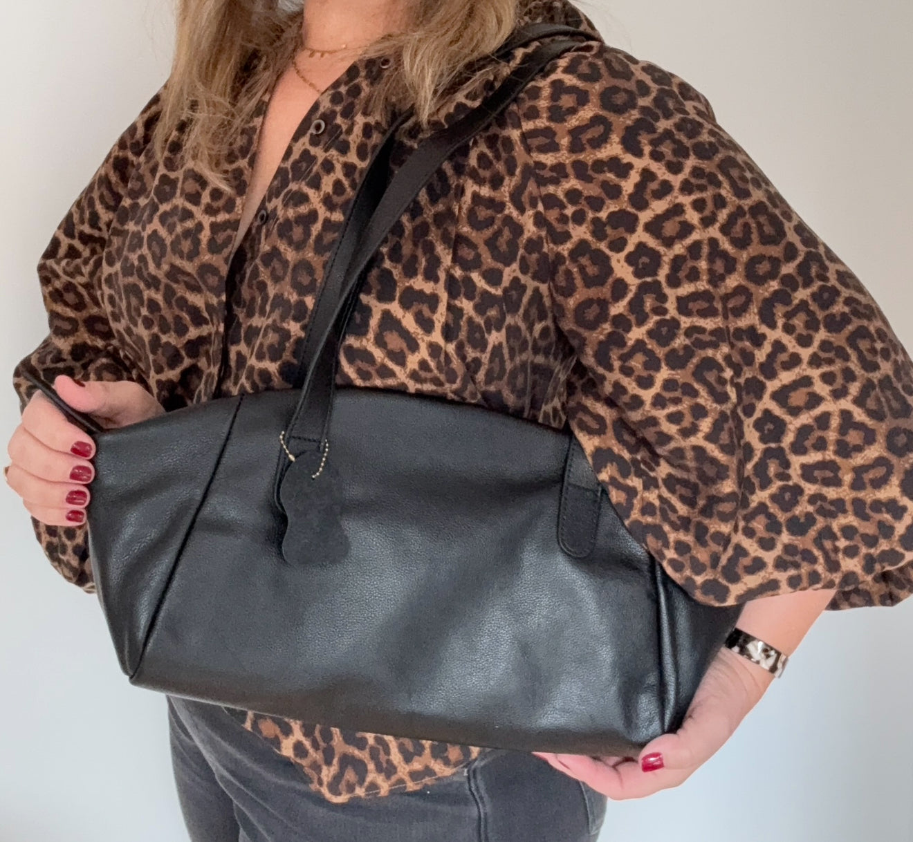 woman holding a black leather bag wearing a leopard print top 