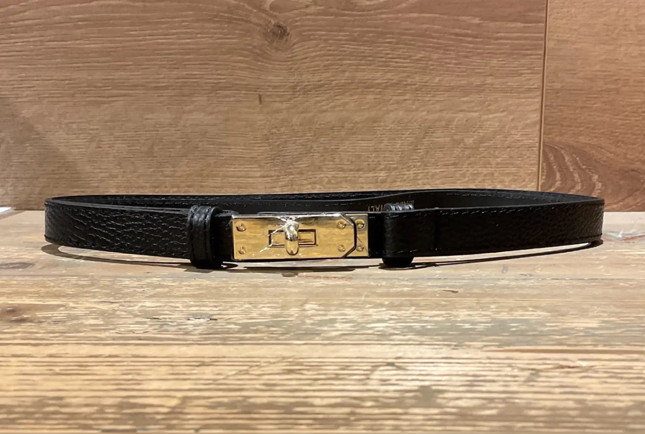 Black narrow leather belt with a gold buckle on a wooden surface