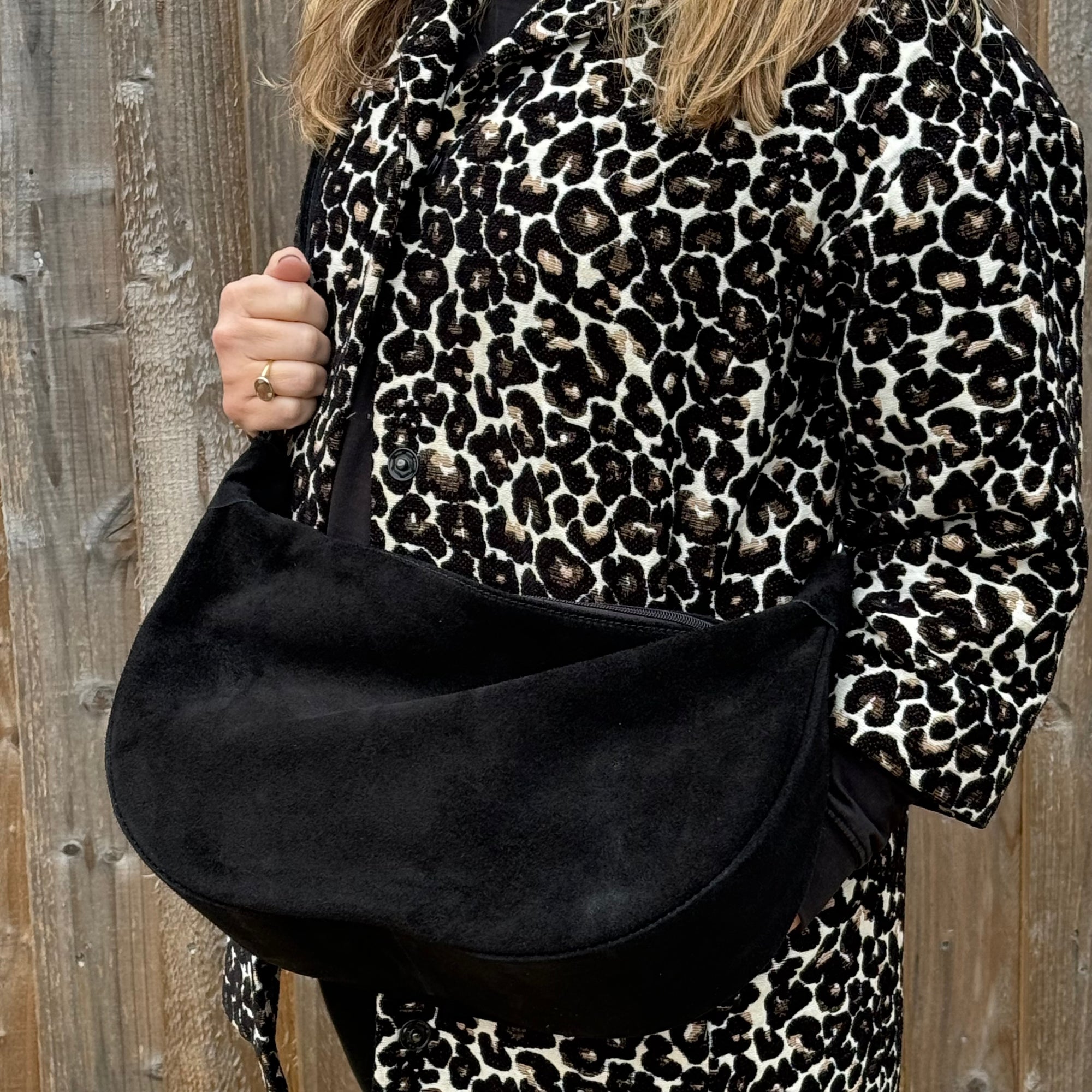 woman wearing a leopard print outfit holding a black suede large crossbody swing  bag 