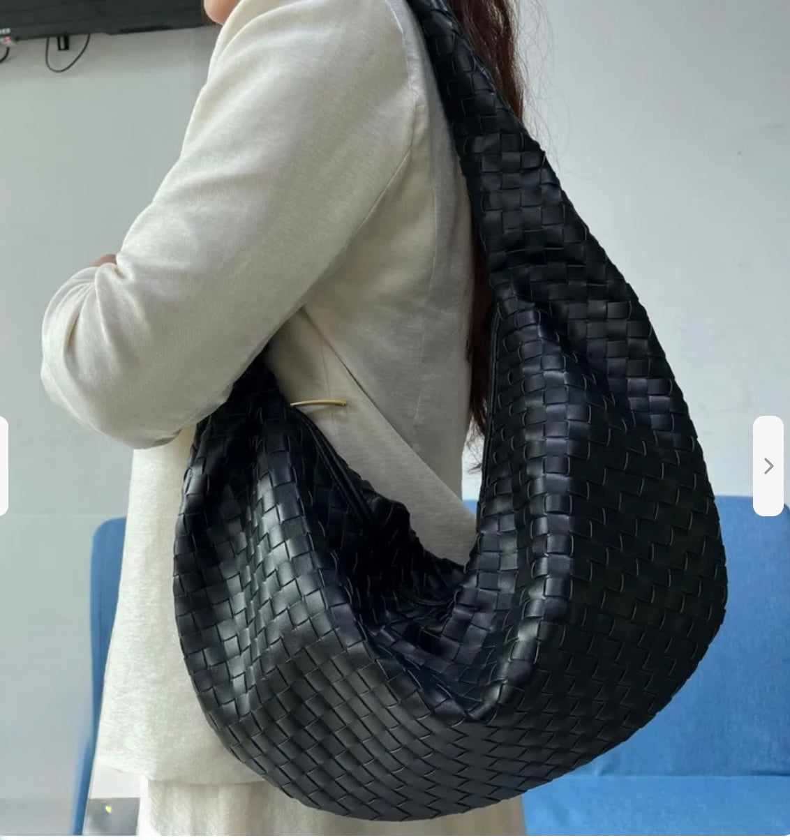 Woman wearing a beige jacket, holding a black woven crossbody handbag. 