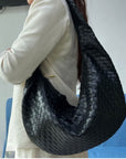 Woman wearing a beige jacket, holding a black woven crossbody handbag. 