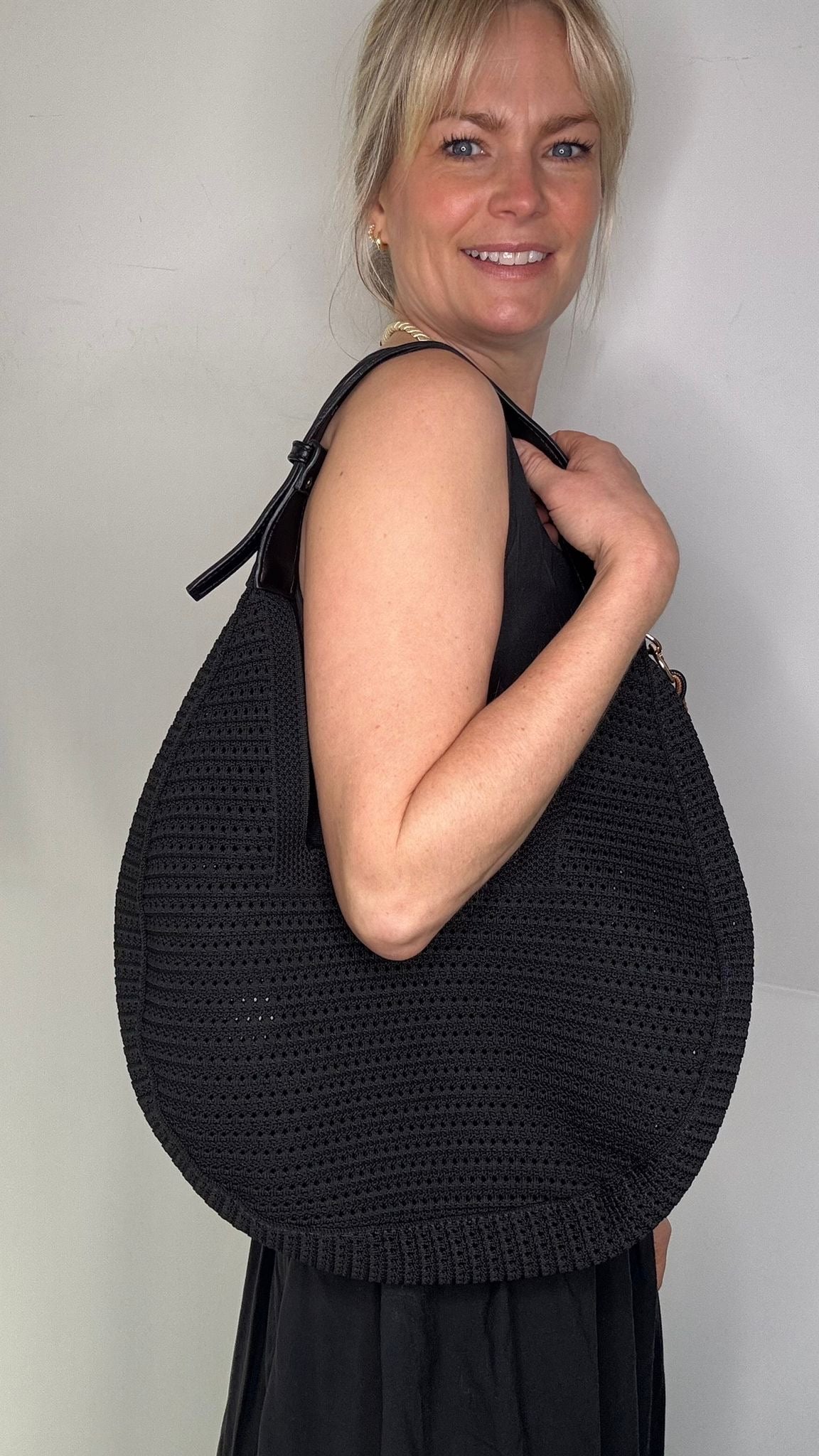 Woman wearing a black dress, holding a black woven handbag. 